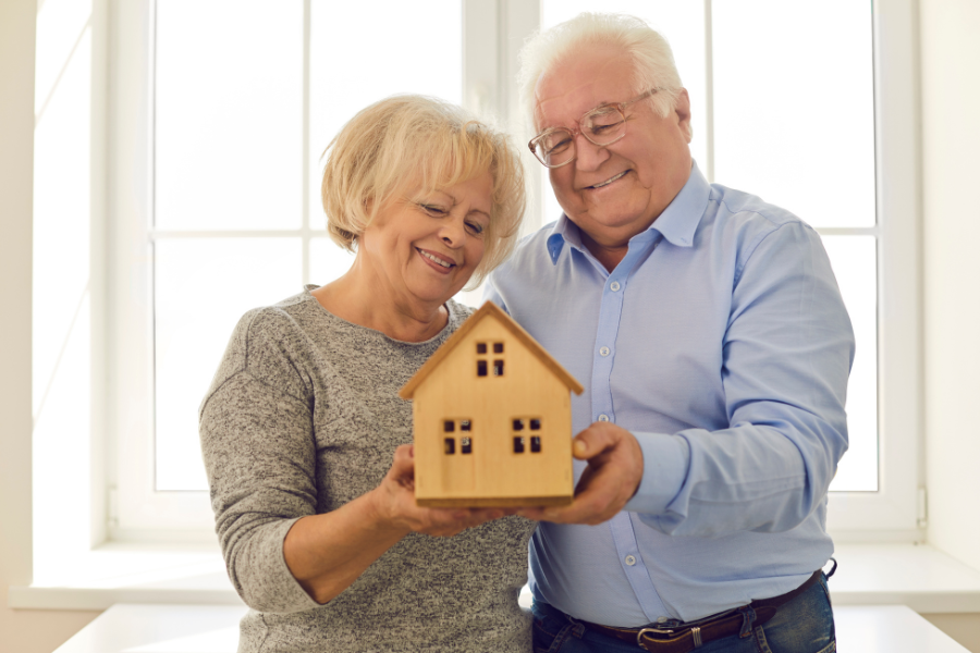 Smiling couple holding a small model house indoors.