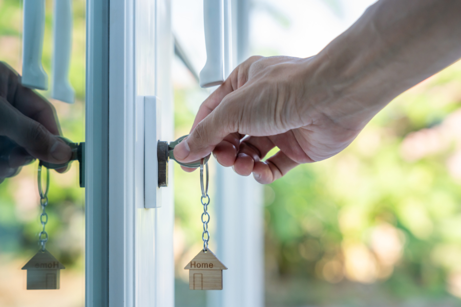 Hand unlocking a door with a keychain shaped like a small house, symbolizing home ownership or moving into a new home.