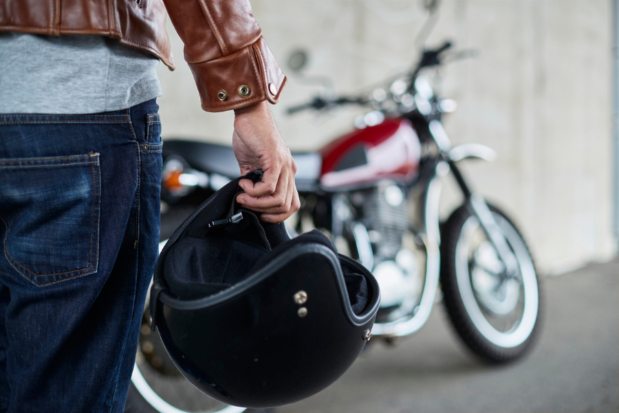 Person holding a motorcycle helmet beside a parked motorcycle, suggesting preparation for a ride or motorcycle ownership.