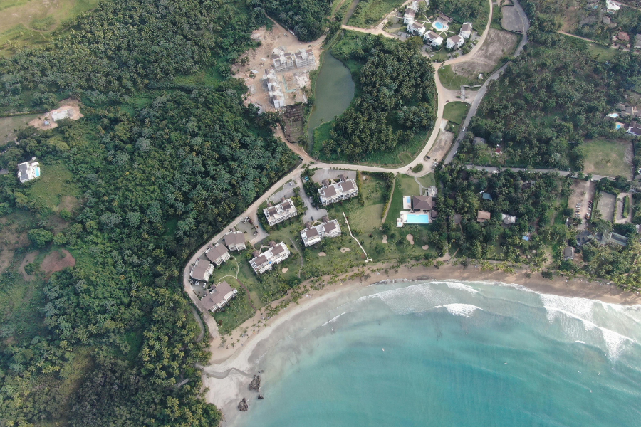 Aerial view of coastal homes, trees, and shoreline near turquoise water.