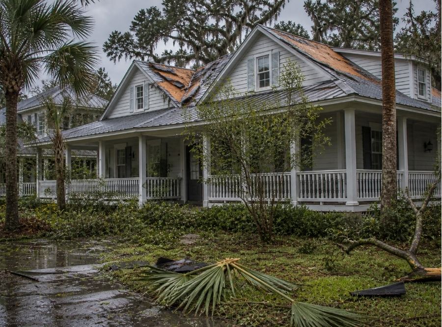 Bluffton, South Carolina home after a coastal storm, showing visible roof damage, scattered debris, and wet surroundings.