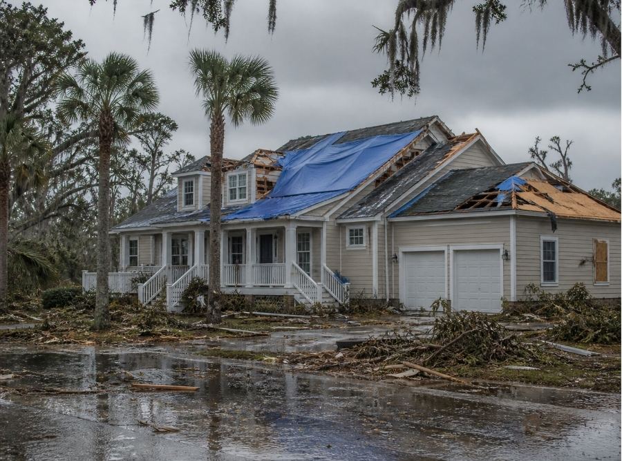 South Carolina post-hurricane residential scene showing a damaged home with visible roof damage, debris in the yard, and water intrusion signs.