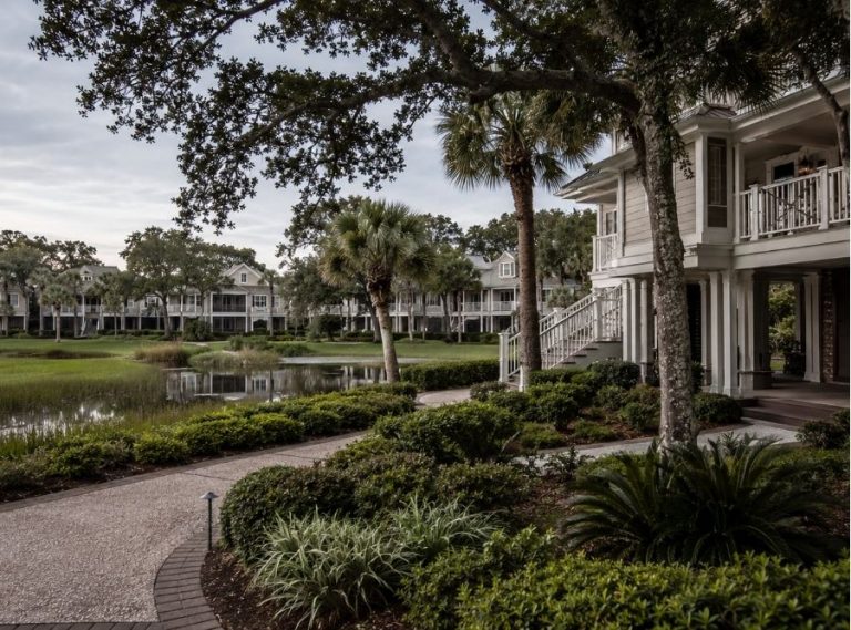 Upscale Hilton Head Island villa community in a resort setting, inspired by Sea Pines, Palmetto Dunes, or Shipyard Plantation, with Lowcountry architecture, palm trees, live oaks, lagoon or golf-course surroundings, and subtle coastal atmosphere