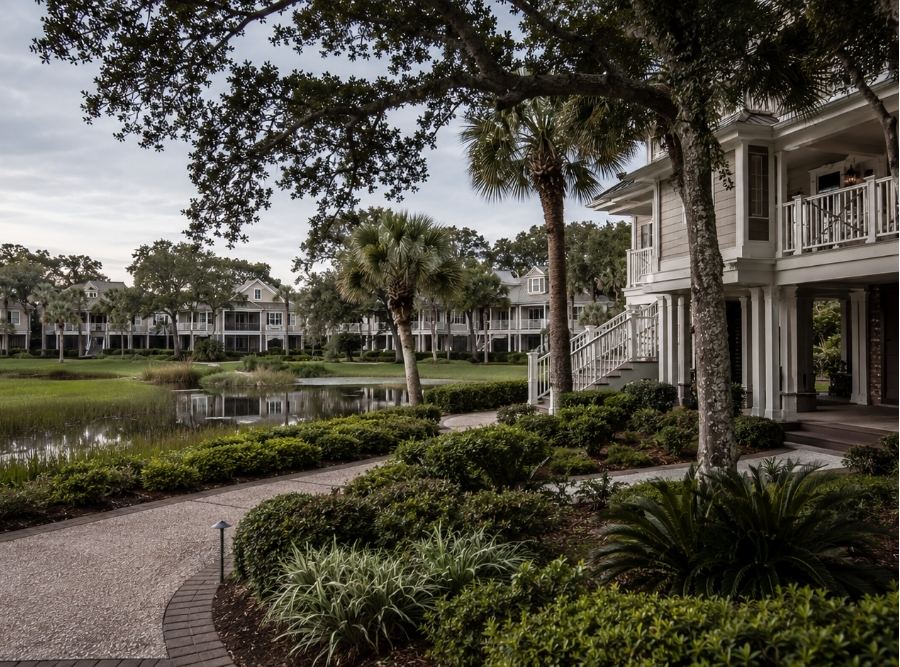 Upscale Hilton Head Island villa community in a resort setting, inspired by Sea Pines, Palmetto Dunes, or Shipyard Plantation, with Lowcountry architecture, palm trees, live oaks, lagoon or golf-course surroundings, and subtle coastal atmosphere