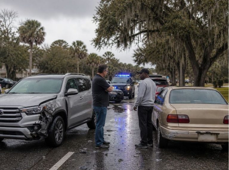 roadside scene in Bluffton, South Carolina after a multi-vehicle accident on a road resembling US-278. One vehicle shows moderate damage while another older vehicle appears uninsured. A driver stands beside their car looking concerned, speaking with another driver
