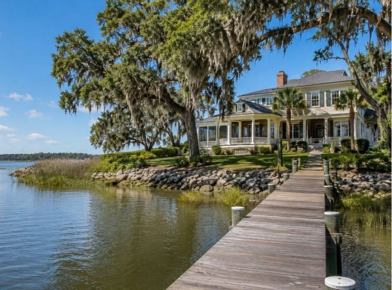 Luxury waterfront home in Beaufort, SC with a private dock, calm coastal water, and live oak trees draped in Spanish moss under a clear blue sky.